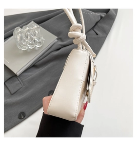 Detail of cream white shoulder bag featuring textured faux leather and a knotted strap detail