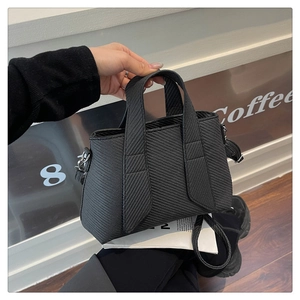 Detail of black tote bag featuring herringbone texture and detachable shoulder strap