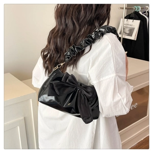 Detail of black bow shoulder bag with glossy finish and ruffled strap on model