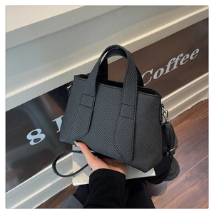 Close-up of black tote bag with diagonal texture shown in a coffee shop setting