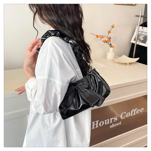 Detail of black glossy leather bag with oversized bow and ruffled shoulder strap
