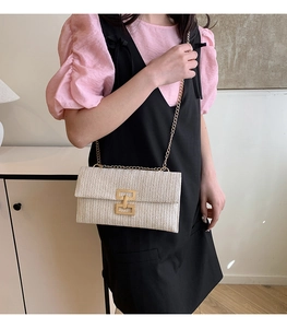 Detail of beige woven straw clutch bag with gold geometric metal buckle and chain