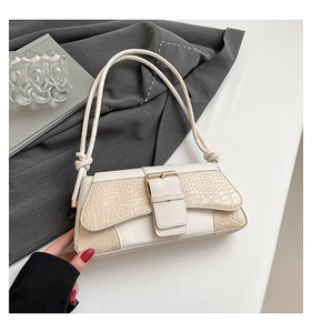 Detail of cream baguette bag featuring faux crocodile texture and knotted shoulder strap