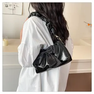 Detail of a black shiny crossbody bag with a large bow and ruched cloud shoulder strap