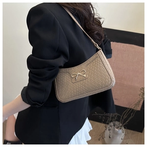 Gros plan sur la texture tissée et le nœud doré du sac baguette en similicuir beige