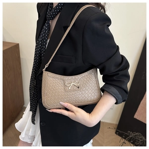 Détail du sac croissant tressé kaki avec boucle nœud dorée porté sur un blazer