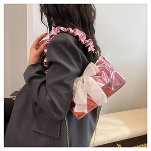 Detail view of pink bow shoulder bag with metallic texture and gold chain on model