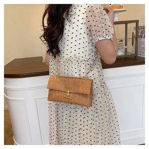 Detailed view of woven straw shoulder bag with gold chain strap and square buckle on floral dress