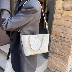 White quilted tote bag with gold chain strap carried by a model in a grey suit