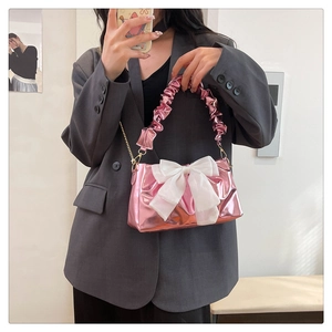 Close-up of a pink glossy handbag featuring a large white bow and gold chain strap