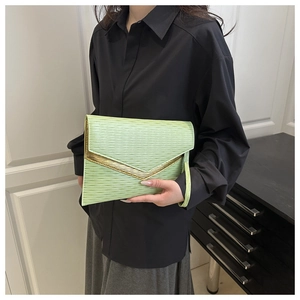 Detail of green pleated envelope clutch bag featuring gold trim and wrist strap