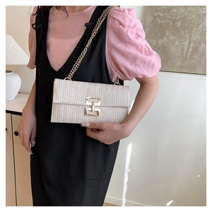 Detail of a beige straw woven crossbody bag with gold chain strap on a model