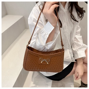 Sac baguette marron tressé avec nœud doré porté par un mannequin en décor minimal