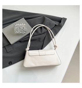 Detail of creamy white baguette bag with knotted straps on a gray suit background