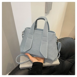 Detail of light blue woven texture tote bag with silver hardware on a display stand