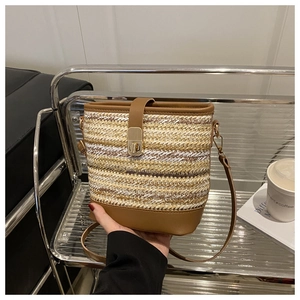 Detail of woven straw bucket bag with brown leather trim and golden metal clasp