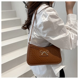 Détail du sac bandoulière marron tressé avec fermoir nœud doré porté par le mannequin