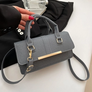 Chic grey textured crossbody bag with gold hardware and woven handle on white table
