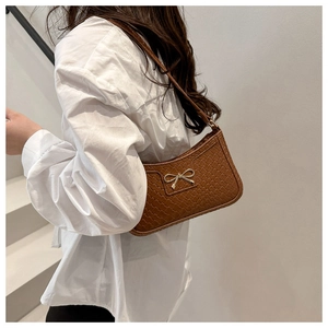 Détail d'un sac porté épaule en texture tressée marron avec nœud en métal argent