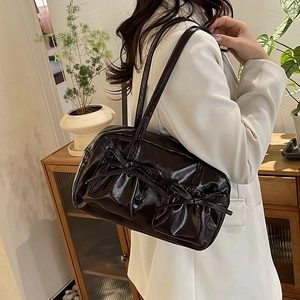 Sac fourre-tout noir brillant avec nœuds porté à l'épaule sur un blazer blanc chic