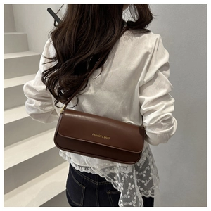 Detailed close-up of dark brown leather underarm bag with gold logo on a white lace top