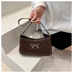 Détail d'un sac à main tressé avec boucle nœud dorée et poignée supérieure fine