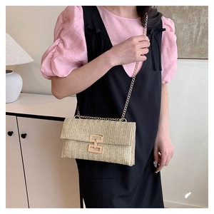 Detail of woven straw handbag featuring golden metal buckle and chain shoulder strap