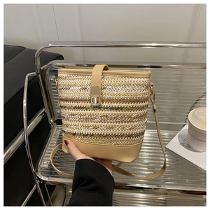 Detail of woven straw bucket bag showing leather base and gold twist lock closure