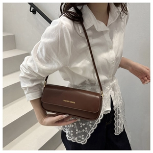 Detail of a dark brown leather underarm bag with gold lettering on a white background