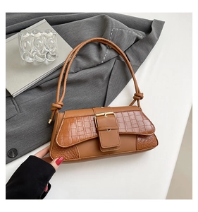 Close-up of brown croc-embossed underarm bag with gold metal buckle on grey blazer