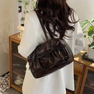 Détail du sac bandoulière en similicuir marron foncé avec nœuds décoratifs et texture plissée