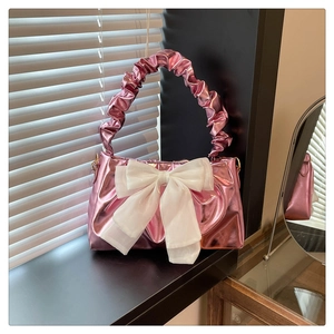 Detailed view of pink metallic crossbody bag featuring a large white bow and pleated handle