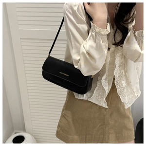 Detail of minimalist black baguette bag with gold lettering shown on model shoulder