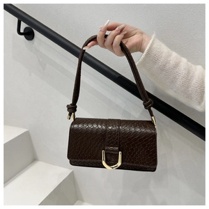 Detailaufnahme einer dunkelbraunen Tasche mit Krokoprägung und goldener Hufeisenschnalle