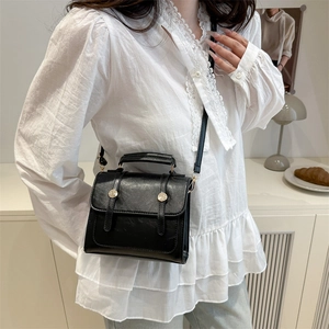 Vintage black crossbody square bag with gold buckle and top handle in a cozy setting