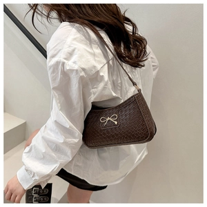 Détail du sac bandoulière marron foncé aspect crocodile avec boucle nœud doré sur mannequin