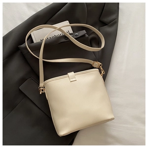 Close-up of cream PU leather bucket bag with gold-tone hardware on a grey blazer