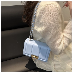 Détail du sac à rabat bleu clair avec fermoir rotatif doré et bandoulière en chaîne