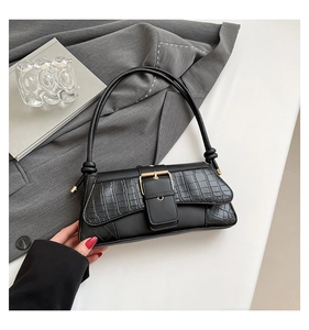 Detail of black faux leather baguette bag with crocodile texture and gold square buckle