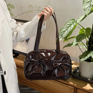Sac fourre-tout en cuir verni marron foncé avec nœuds portés par un modèle en blazer blanc