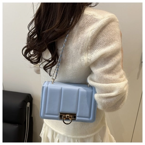 Détail du sac bandoulière matelassé bleu clair avec chaîne dorée sur un pull blanc élégant