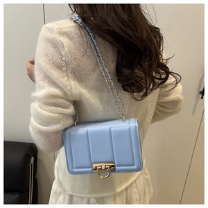 Détail du sac bandoulière bleu clair avec boucle en U dorée et motifs géométriques