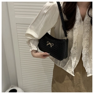 Détail d'un sac bandoulière tressé noir avec boucle nœud doré et texture raffinée