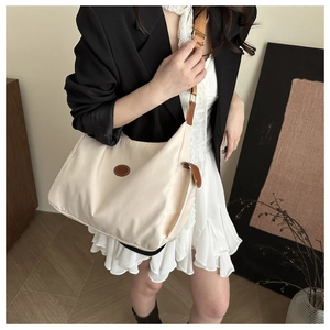 Close-up of beige crossbody bag with brown leather details on a model in home setting