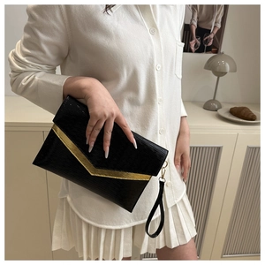 Detail of black envelope clutch featuring a gold V-shaped metal trim and wristlet strap