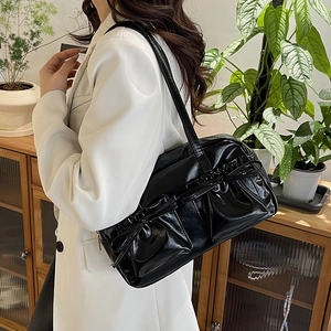 Détail du sac à bandoulière noir brillant avec plis frontaux et décoration de nœud