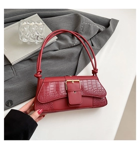 Detail of dark red croc-embossed shoulder bag with golden buckle and knotted strap