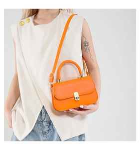 Fashionable bright orange tote bag with gold square buckle shown on an elegant model