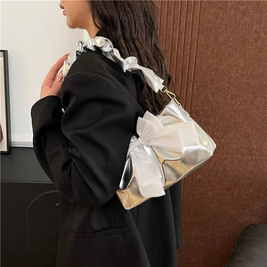 Silver metallic shoulder bag with oversized white bow and pleated strap on a blazer