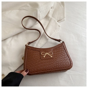 Gros plan du sac bandoulière en cuir tressé marron avec boucle papillon dorée
